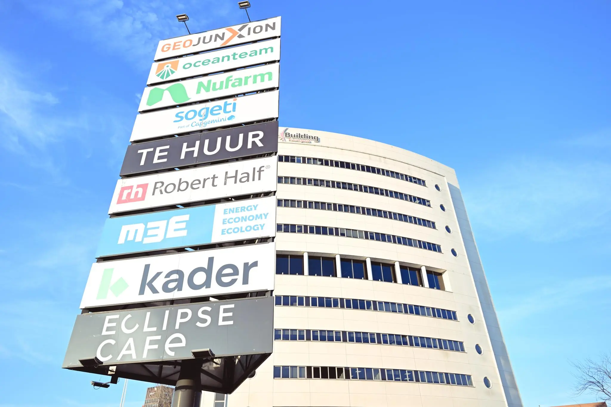 Bedrijvensigning met namen van huurders voor het kantoorgebouw Rivium Quadrant tegen een heldere blauwe lucht.